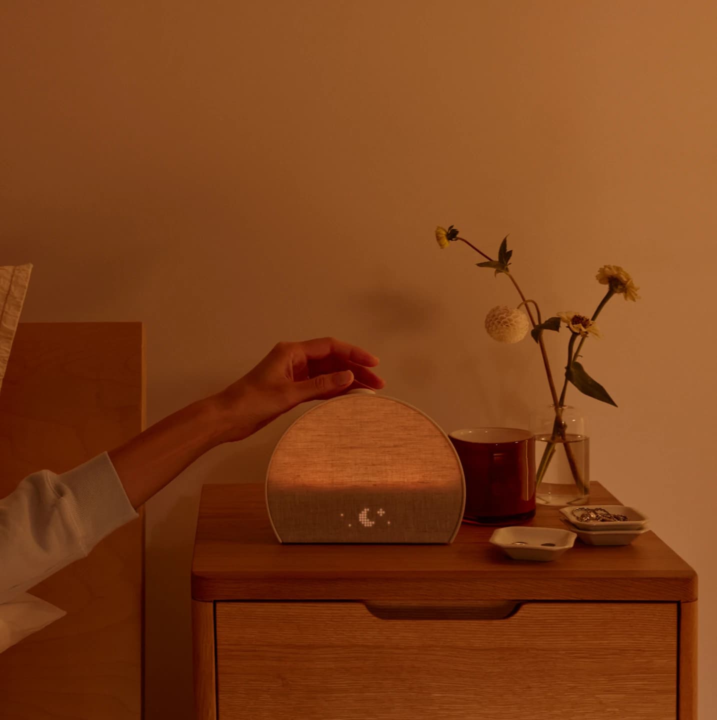 Hand tapping the top button of a Restore 3 on a nightstand