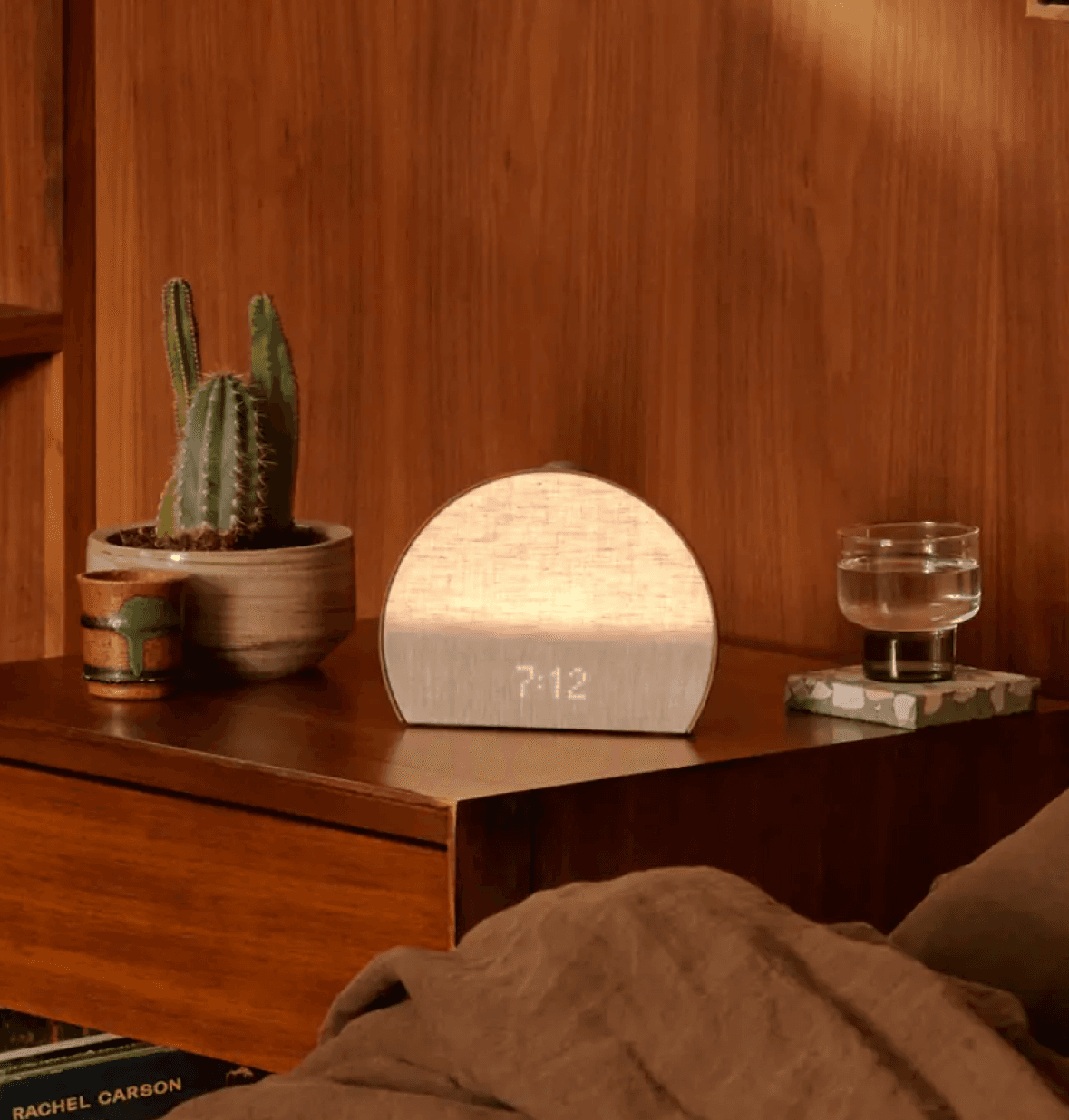 Hatch sleep clock cocoa on a nightstand next to a cup of water and a cactus