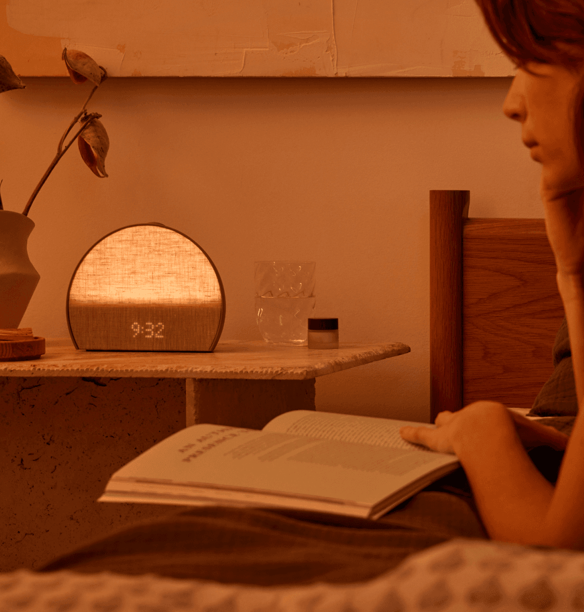 Hatch sleep clock greige next to a woman reading on a bed